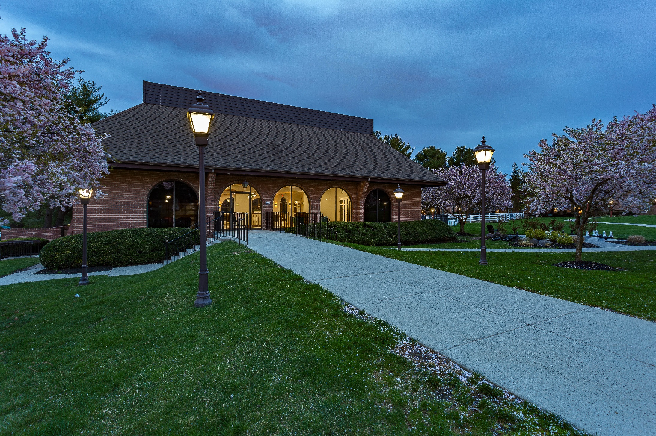 Exterior of Clubhouse, showing lit walkways and landscaped grass and hedges.